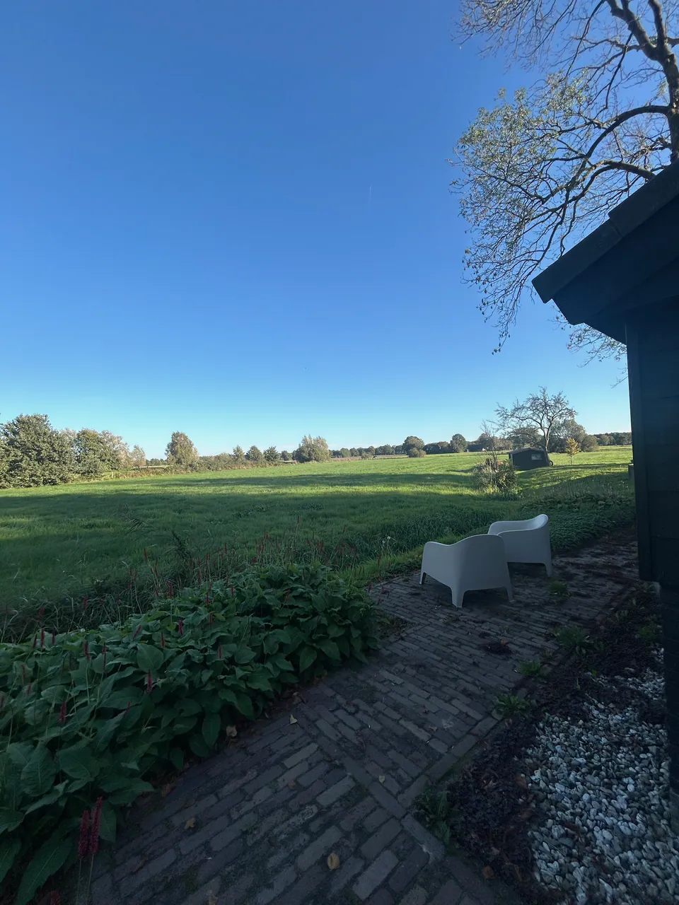 Het terras met twee witte stoelen aan de rand van het weiland, met vrij uitzicht over het land.